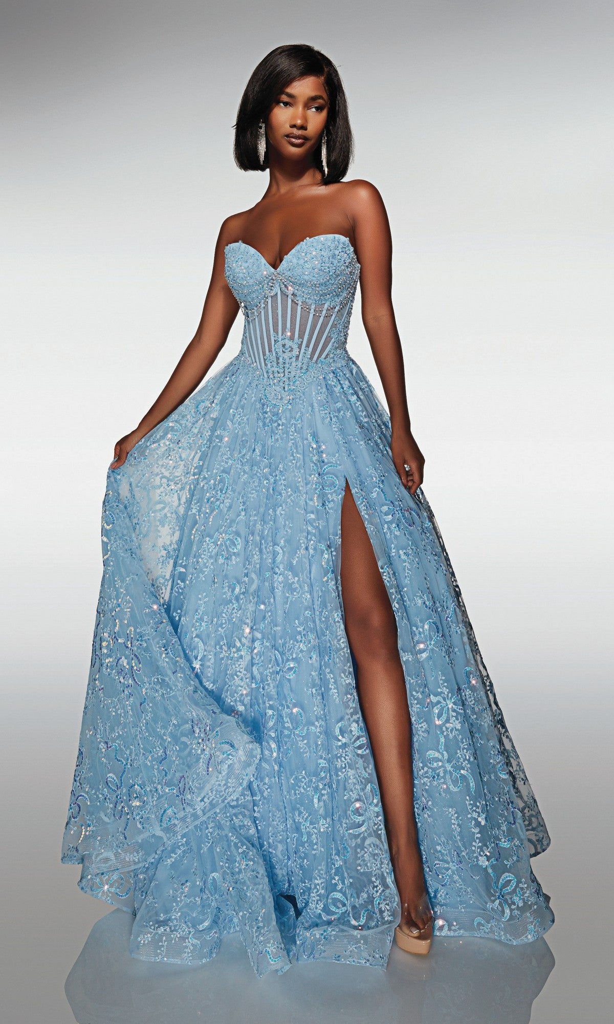 A woman in the Alyce 62033 long formal dress in glacier blue, featuring a strapless beaded corset bodice, floral embroidery, and a thigh-high slit, stands against a plain gradient background.